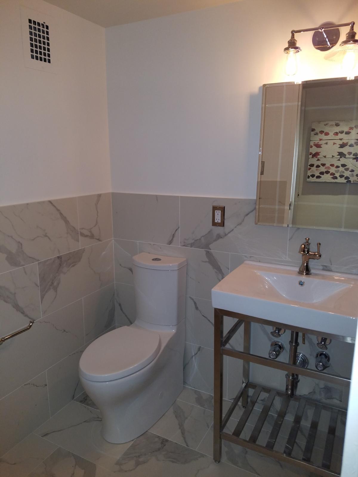 Bathroom renovation — large-format marble porcelain tile, chrome console vanity and industrial light fixture