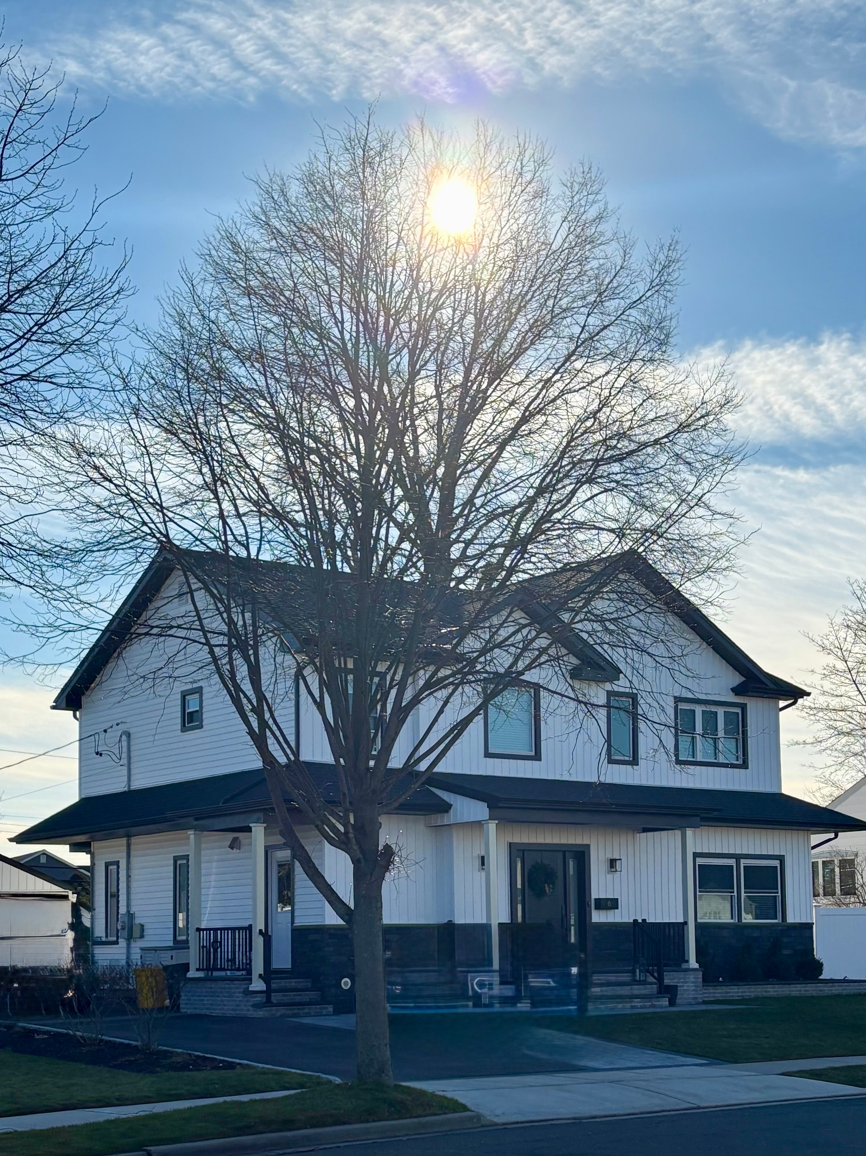 Full home exterior — white board-and-batten with sunburst gable detail and mature tree